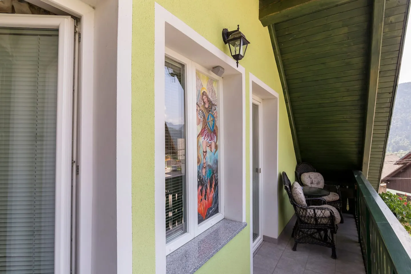 Balkon zelenega apartmaja s pleteno klopjo in stolom